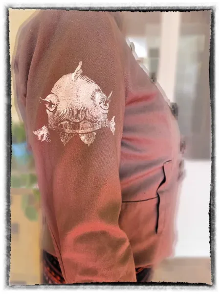 Auf dem Unterarm einer Person ist ein detailliertes, weißes Tattoo eines Fisches zu sehen, das sich von der braunen Haut abhebt und einen natürlichen, lebendigen Eindruck vermittelt.