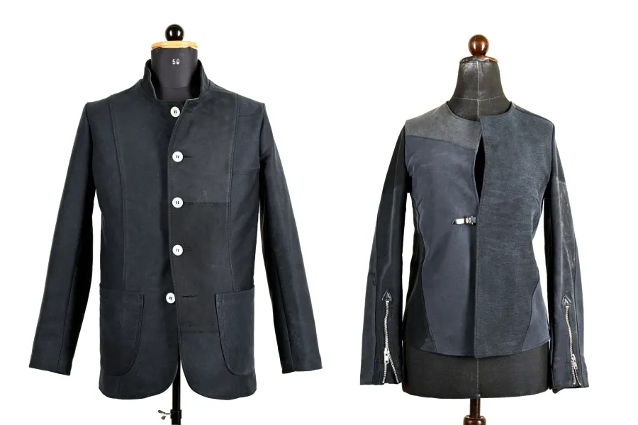 Zwei Kleidungsstücke sind auf Mannequins präsentiert. Das linke Kleidungsstück ist eine dunkle Jacke mit Knöpfen und großen Taschen. Das rechte Kleidungsstück ist eine graue Jacke mit Reißverschlüssen an den Ärmeln und einem asymmetrischen Design.