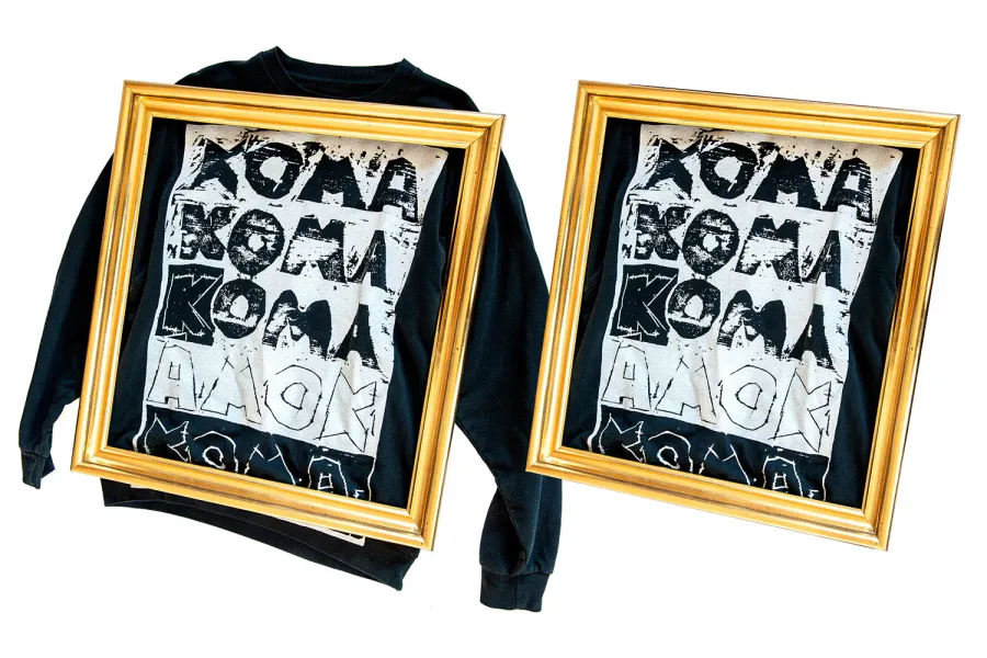 wei gerahmte Bilder zeigen ein schwarzes T-Shirt mit einem auffälligen Druck in weißer und schwarzer Farbe. Der Druck besteht aus großen, grob geschnittenen Buchstaben, die das Wort "KOMMA" in verschiedenen Größen und Schrifttypen darstellen. Die goldenen Rahmen heben die kontrastreichen Motive auf dem T-Shirt hervor.
