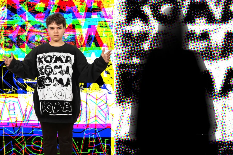 Eine Person steht vor einem farbenfrohen, abstrakten Hintergrund mit geometrischen Mustern und leuchtenden Farben. Die Person trägt einen schwarzen Hoodie mit einem weißen, repetitiven Textdesign, das "KOMA" und "AMOK" zeigt. Die Person hat die Arme ausgebreitet und steht in einer dynamischen Pose.